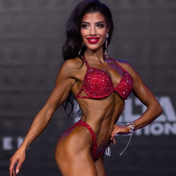 Woman in a red fitness competition outfit posing against a branded backdrop